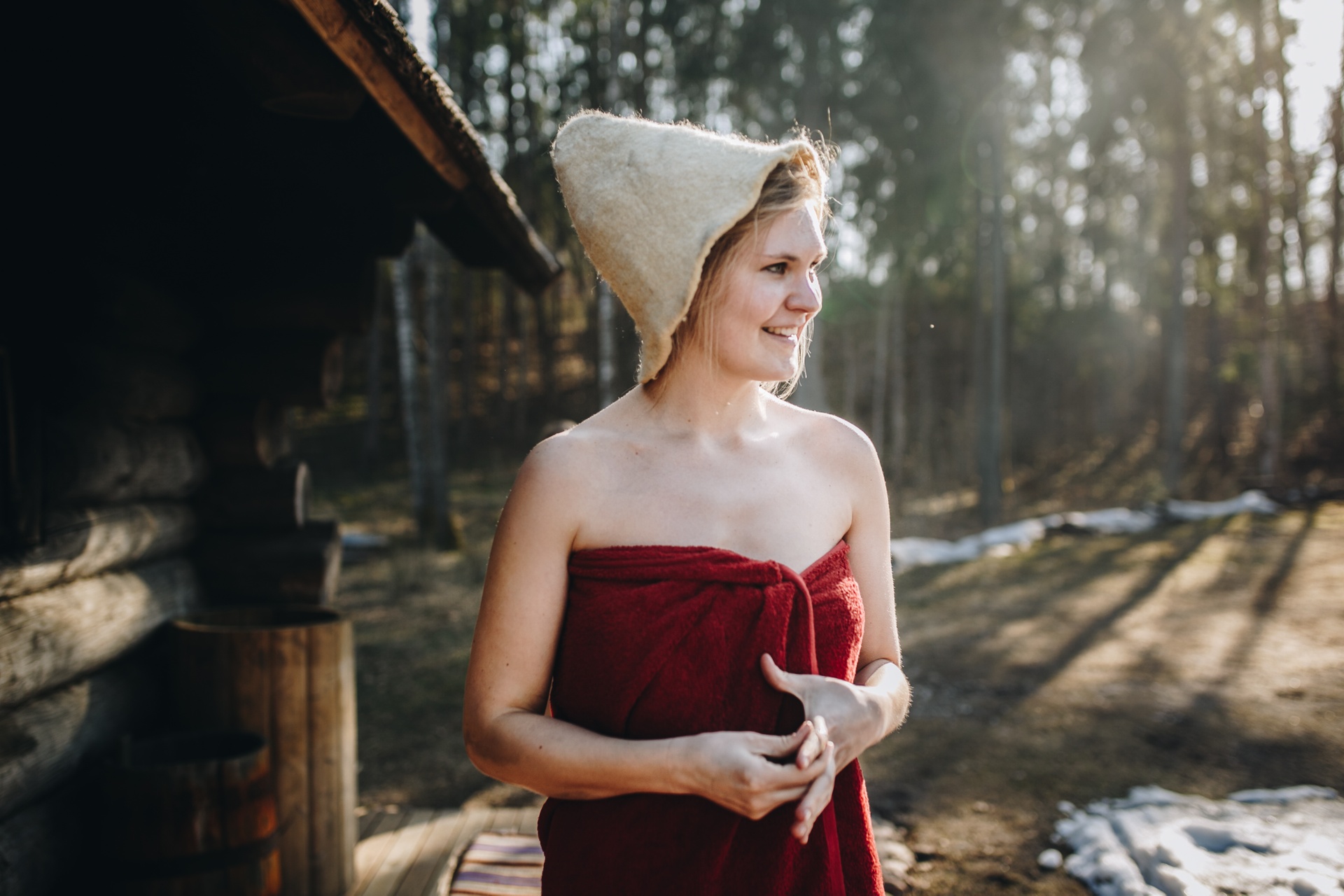Woman with a felt sauna hat and towel outside a smoke sauna