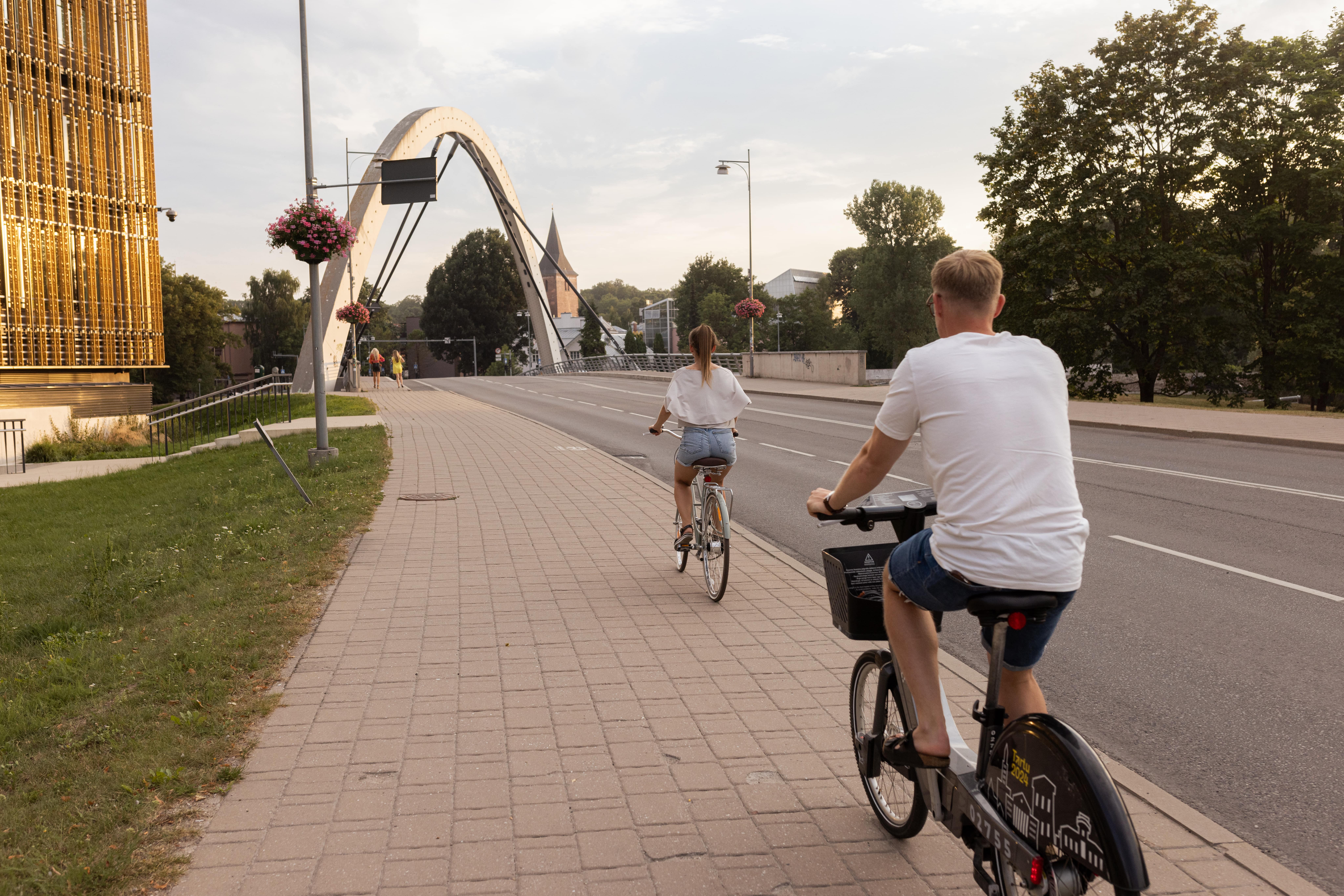 Two people riding bikes in Tartu near the bridge