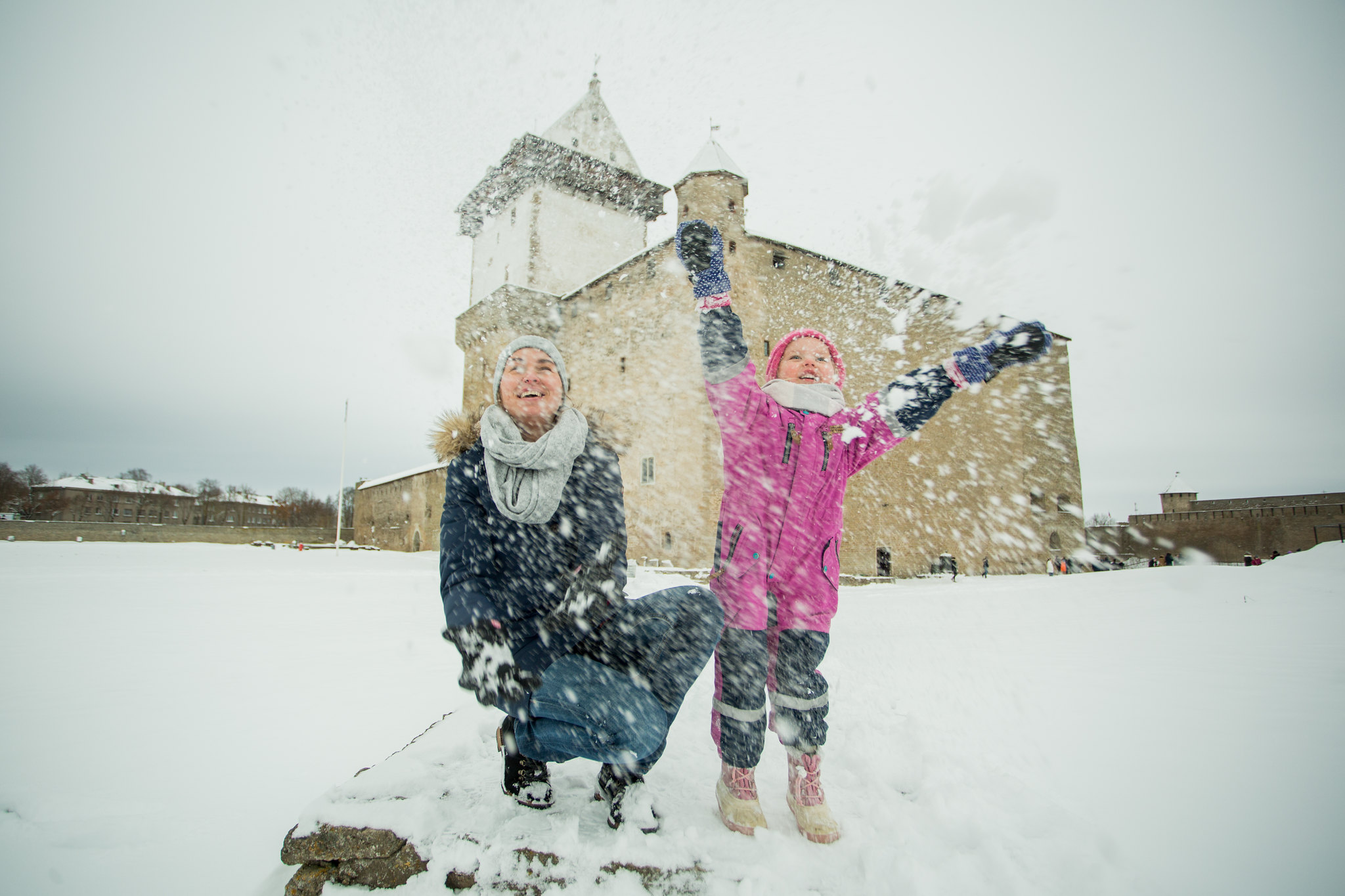 Mother and daughter happily play in the snow by Narva Castle