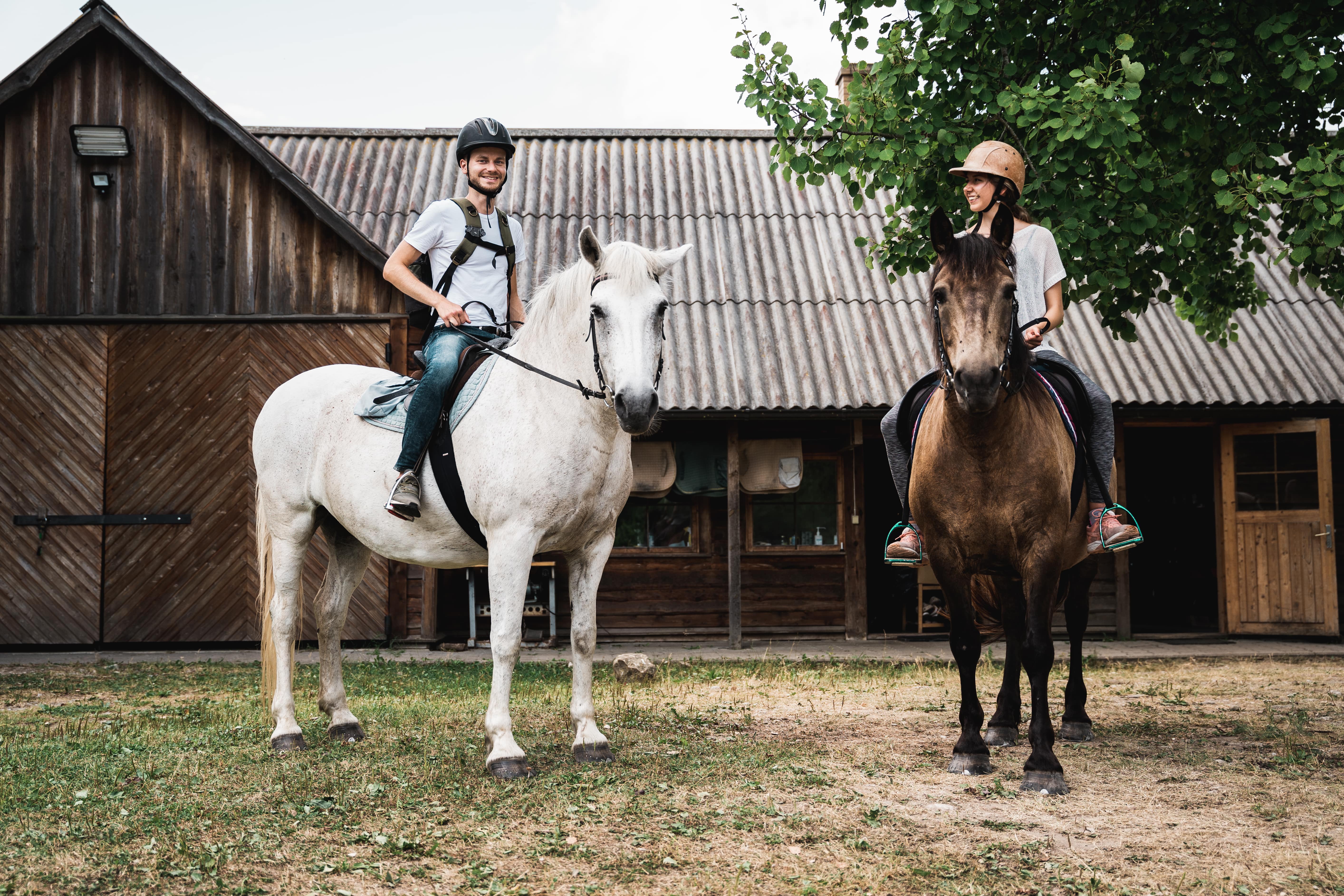 Two people on horseback in front of a wooden barn in Estonia