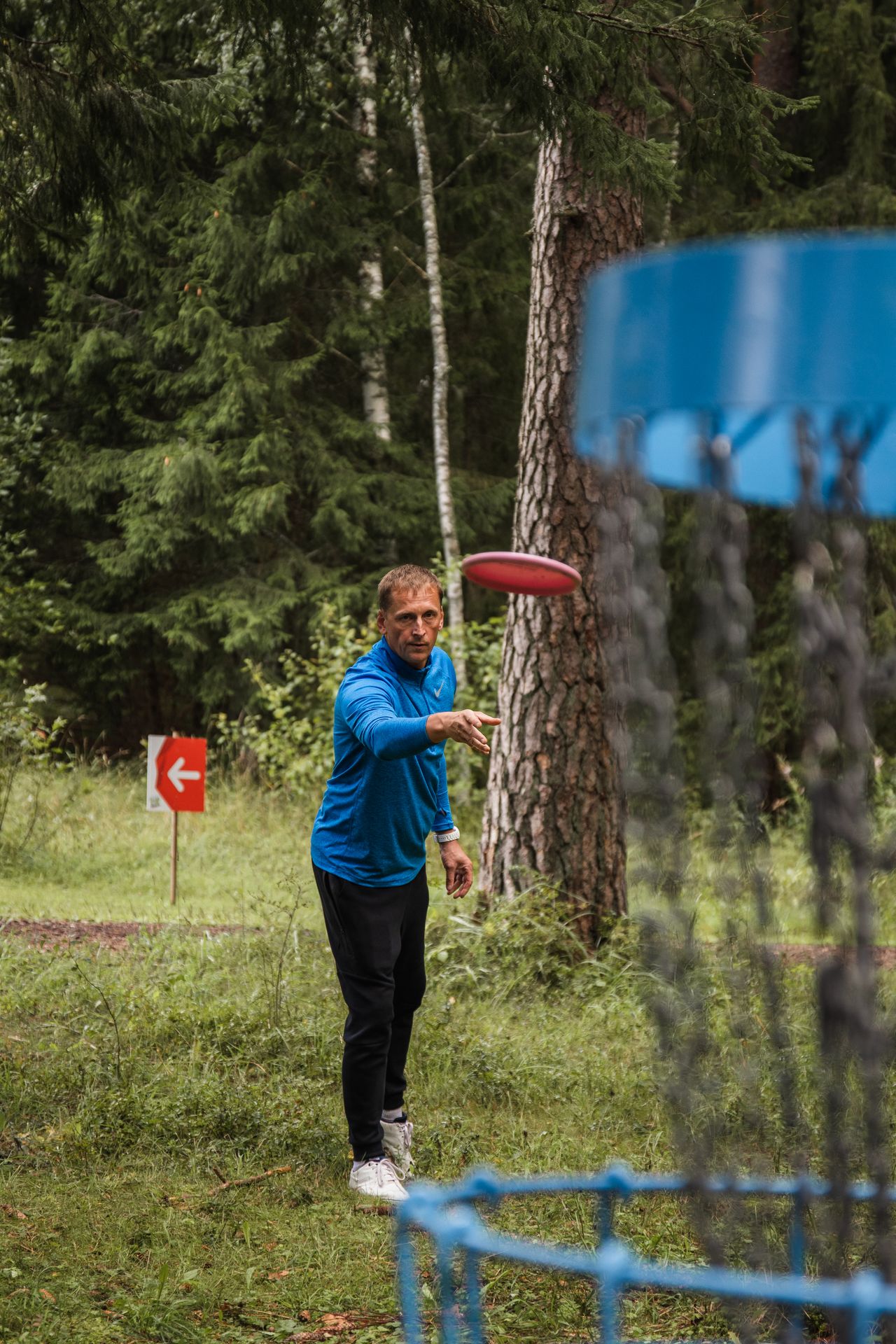 Mies heittämässä frisbeegolf-radalla liitokiekkoa koriin 