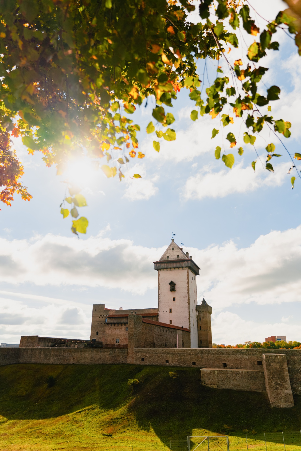 Narva Castle in autumn with sun, clouds, and colored leaves