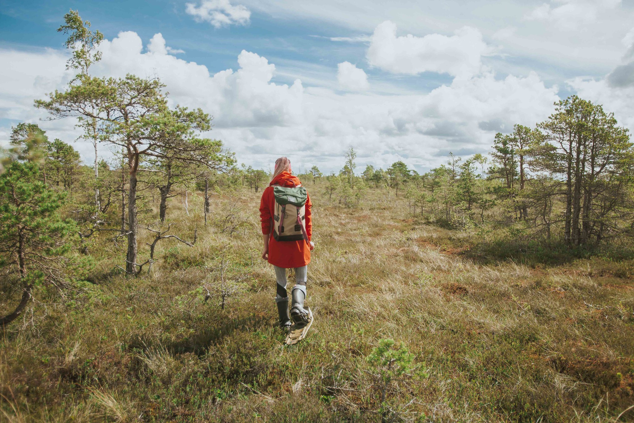 Woman in orange coat wears bogshoes for hiking in Estonia