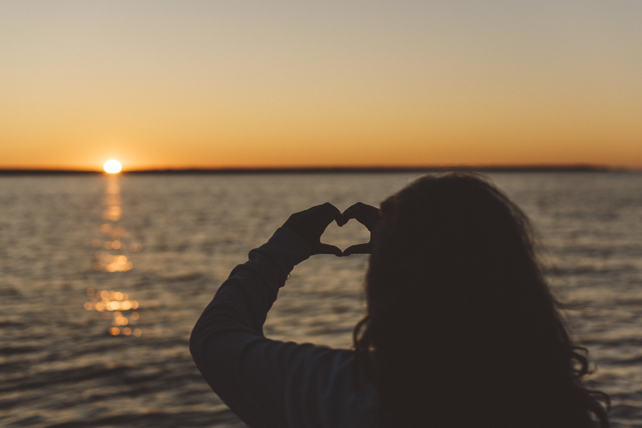 Person does heart hands at sunset over the Baltic Sea