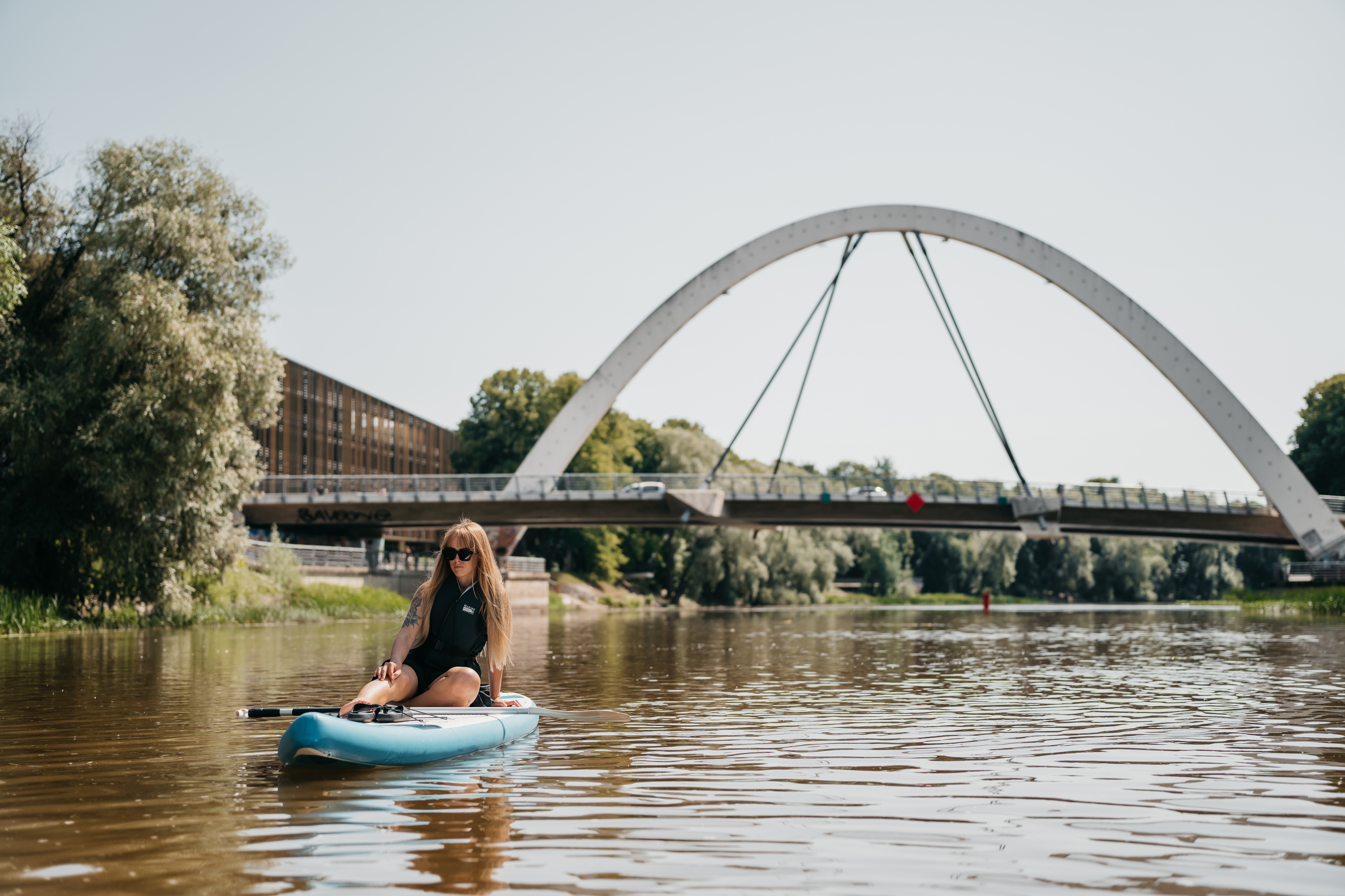 Woman on SUP board near bridge on river in Tartu