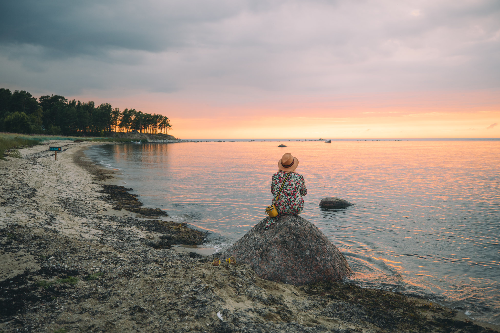 Woman sits on rock and enjoys sunset in West Estonia