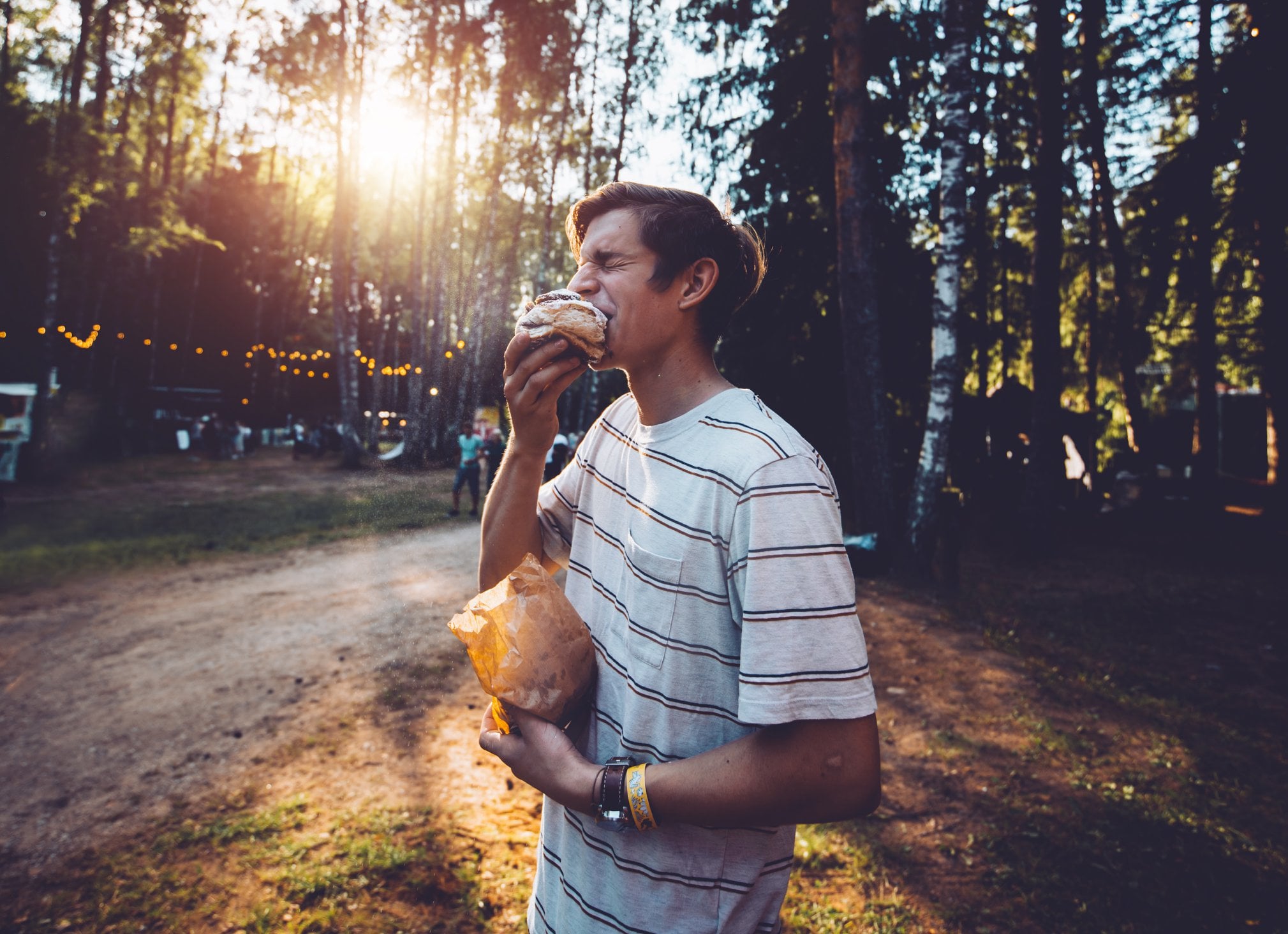 A young man enjoys a large cinnamon roll against a forest