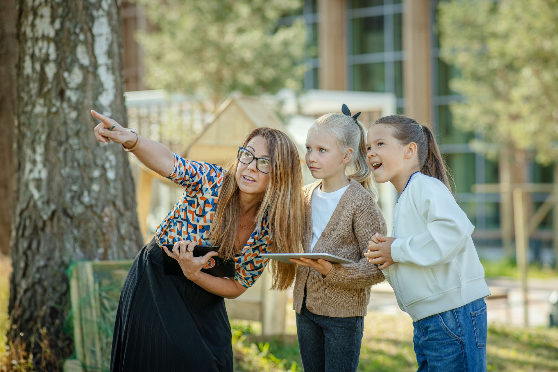 Naine näitab lastele midagi osutades näpuga ja hoides käes tahvelarvutit