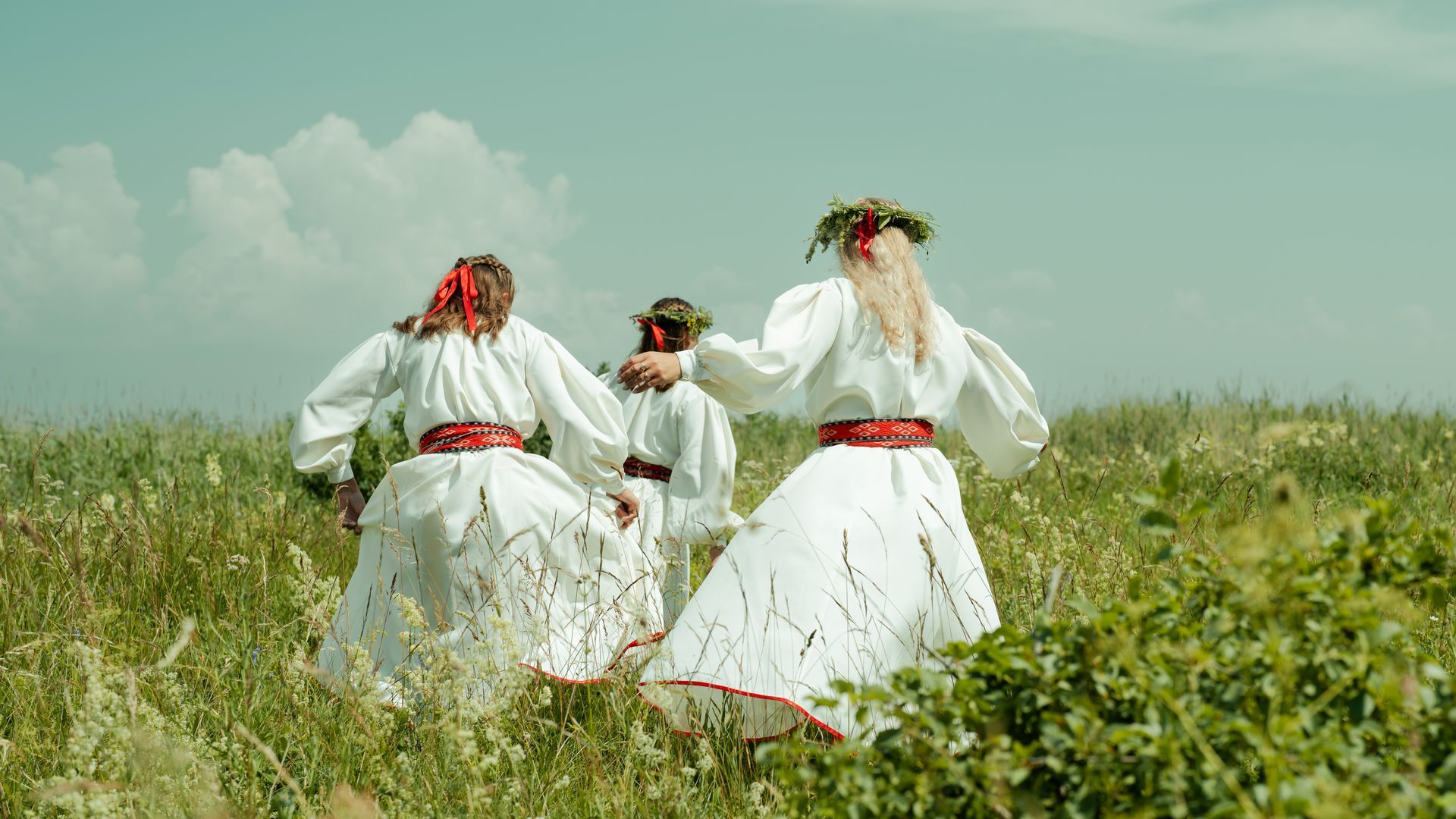 Rahvariietes tüdrukud jooksevad heinamaal