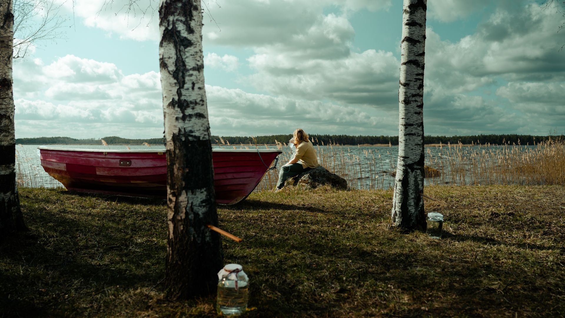 Mees järve kaldal punase paadi kõrval istumas