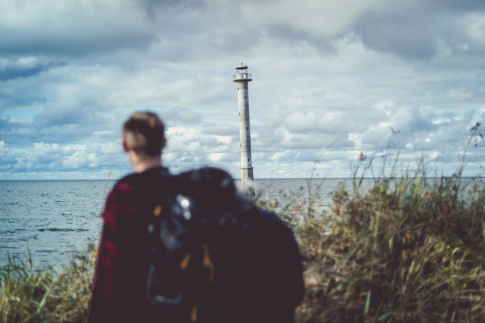 Ein Mann mit Rucksack steht in Harilaid vor dem Leuchtturm Kiipsaare.