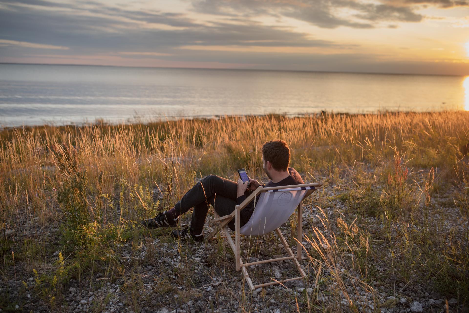 Man sitz in einem Liegestuhl am Meer und benutzt sein Smartphone