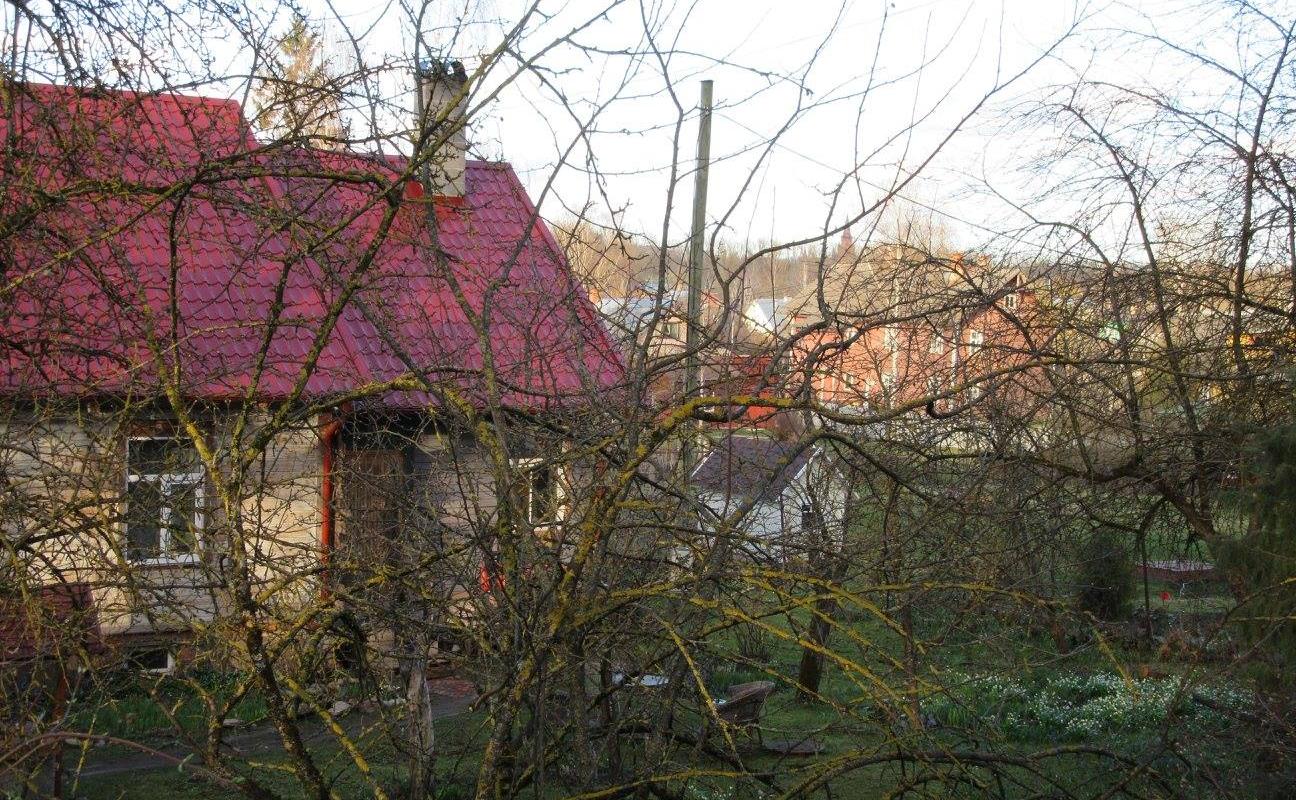 Supilinnas pilsētas daļa ar koka ēkām un brīnišķīgu vidi, aiz kokiem slēpjas koka māja ar sarkanu jumtu
