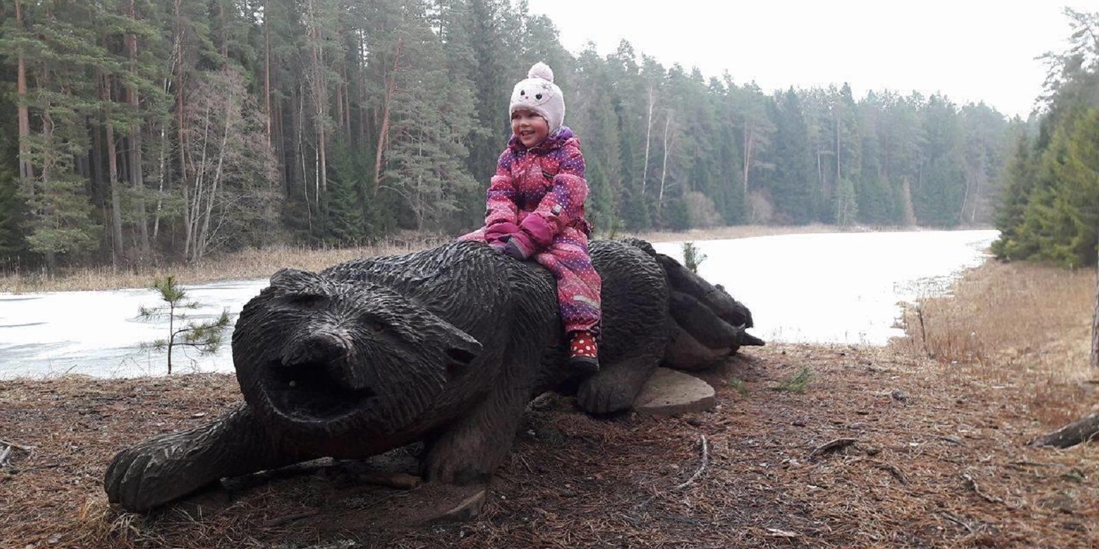 Happy little girl is sitting on the wolf's wooden sculpture