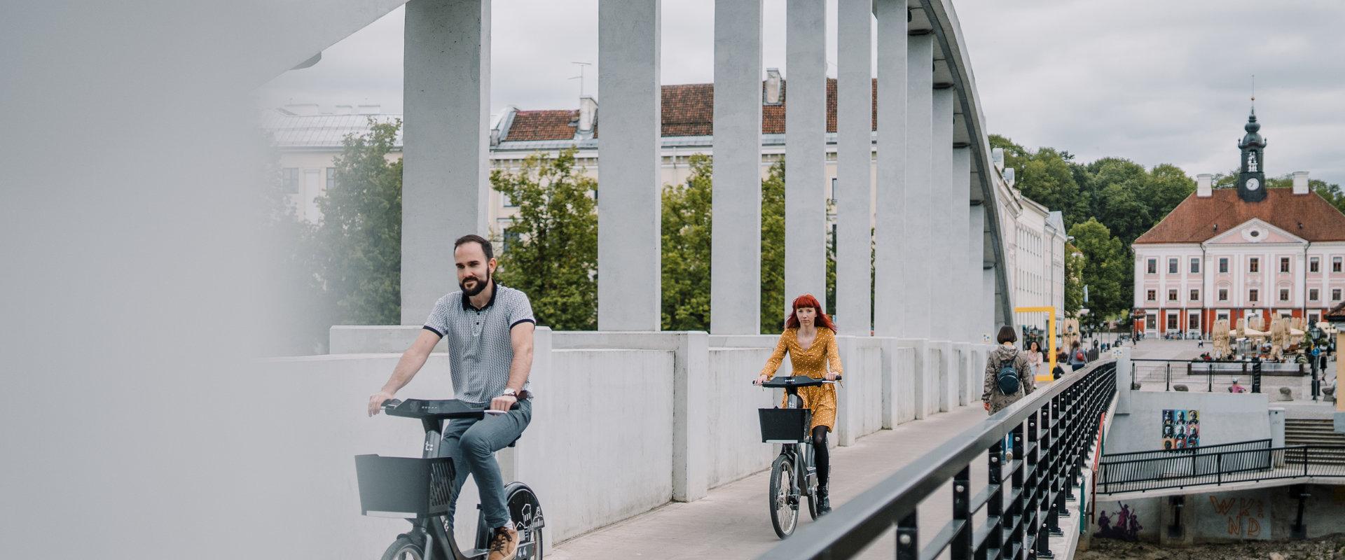 Sommerliche Bogenbrücke und auf Rädern des Tartuer Fahrradverleihs fahrende Jugendliche