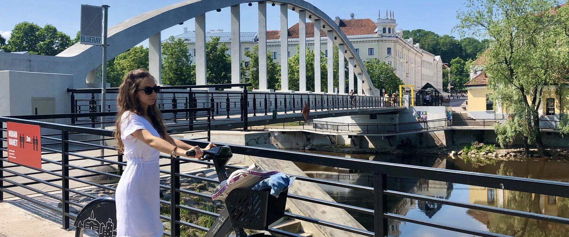 Arch Bridge and a girl standing next to a bike of the Tartu bike sharing circuit