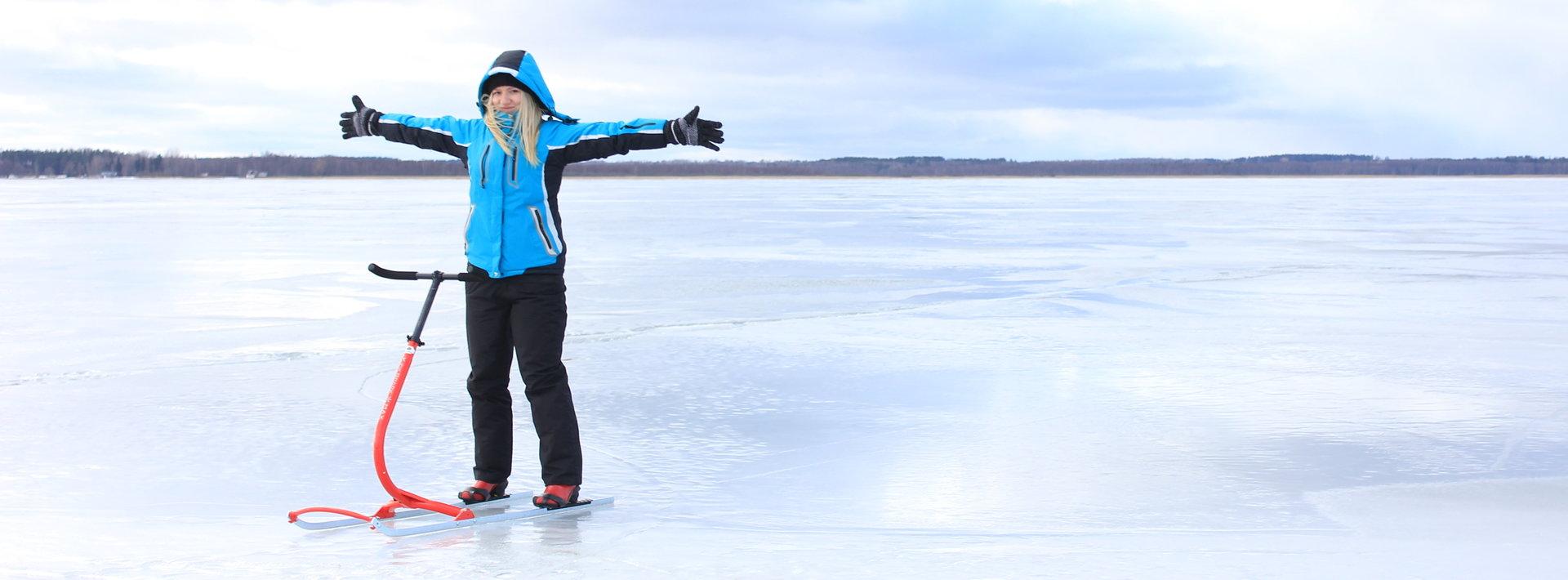 ein Mädchen in der blauen Jacke mit Tretschlitten auf dem Eis des Sees Võrtsjärv