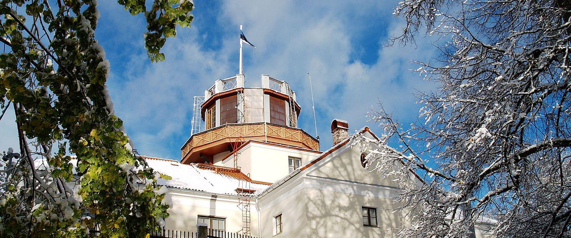 Tartu observatorija sniegotā ziemā, tornī plīvo zili-melni-baltais karogs
