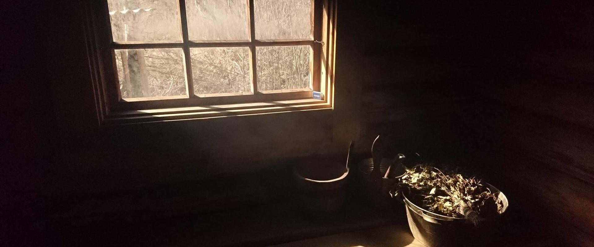 Interior view of the traditional smoke sauna, unlit sauna, light coming from the window and sauna whisks waiting for people