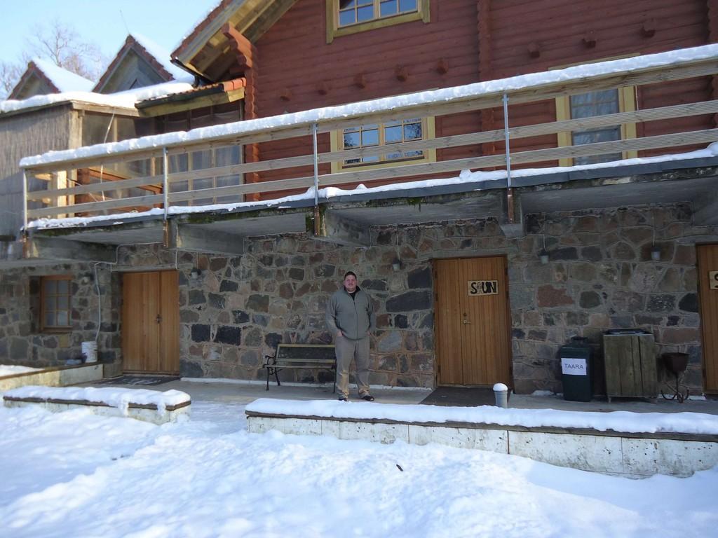 Külaline seisab Lasita Puhkemaja ees Tartumaal, lumisel talvepäeval kivist ja palkidest hoone juures