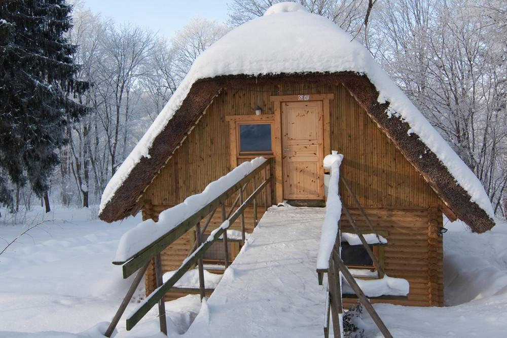Lumega kaetud palkmaja Lasita Puhkemajas Tartumaal, ümbritsetud talvisest metsast ja rahulikust lood