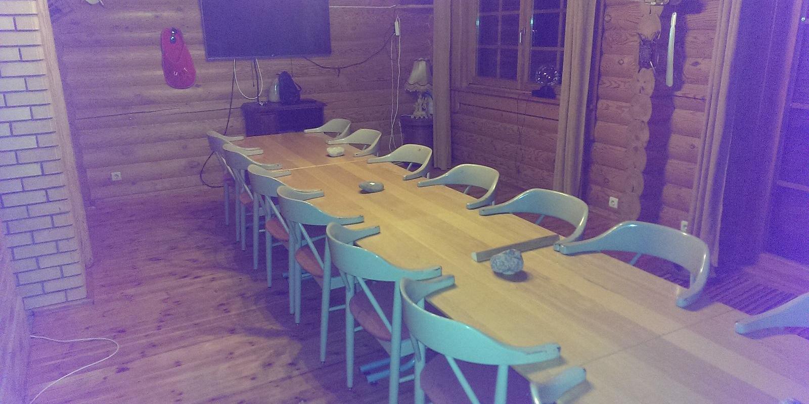 Lasita Puhkemaja hubane peo- ja koosolekuruum Tartumaal, pikk laud toolidega palkseinte vahel.