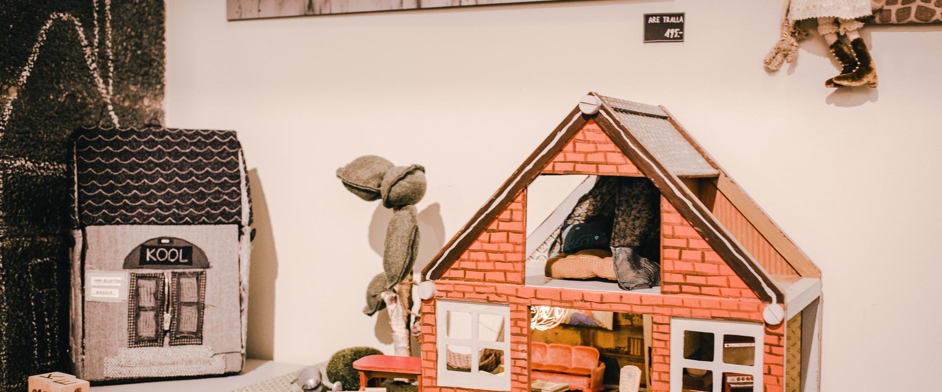 Studio shop Karud ja Pojad playroom: miniature bearhouse and textile schoolhouse, small bears, and a doll. A black-and-white photo of trees and the Emajõgi River on the wall.