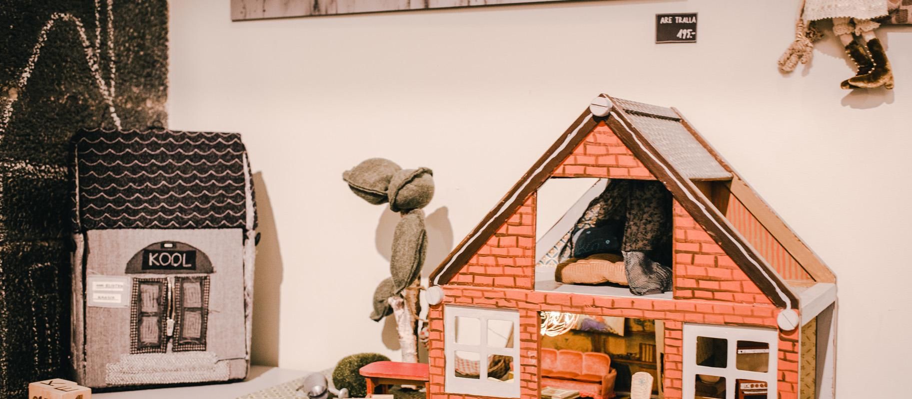 Studio shop Karud ja Pojad playroom: miniature bearhouse and textile schoolhouse, small bears, and a doll. A black-and-white photo of trees and the Emajõgi River on the wall.