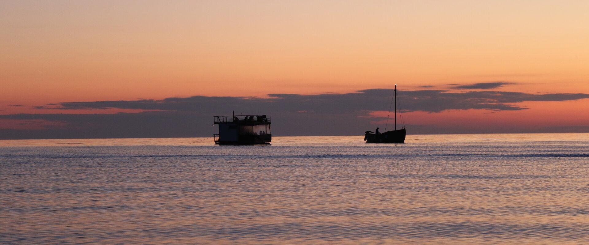 Toilas merel puulaev Tütarsaare Aino ja Meresaun päikeseloojangu taustal