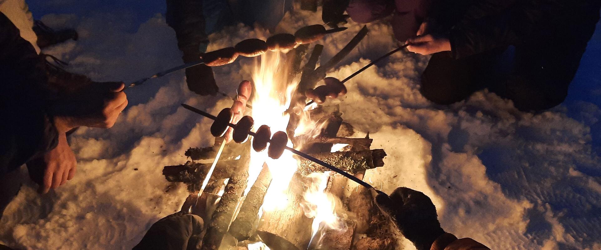 A winter hike ends by the campfire, where warm snacks are cooked on skewers.