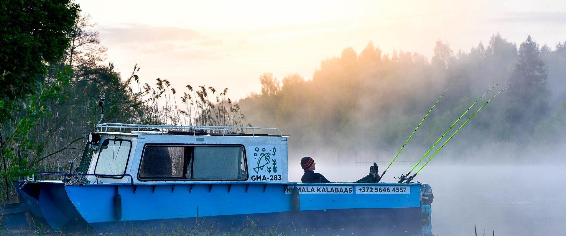 Humala Kalabaasi sinine kalastuspaat seisab udusel järvel, kalamees puhkab ja ootab saaki.