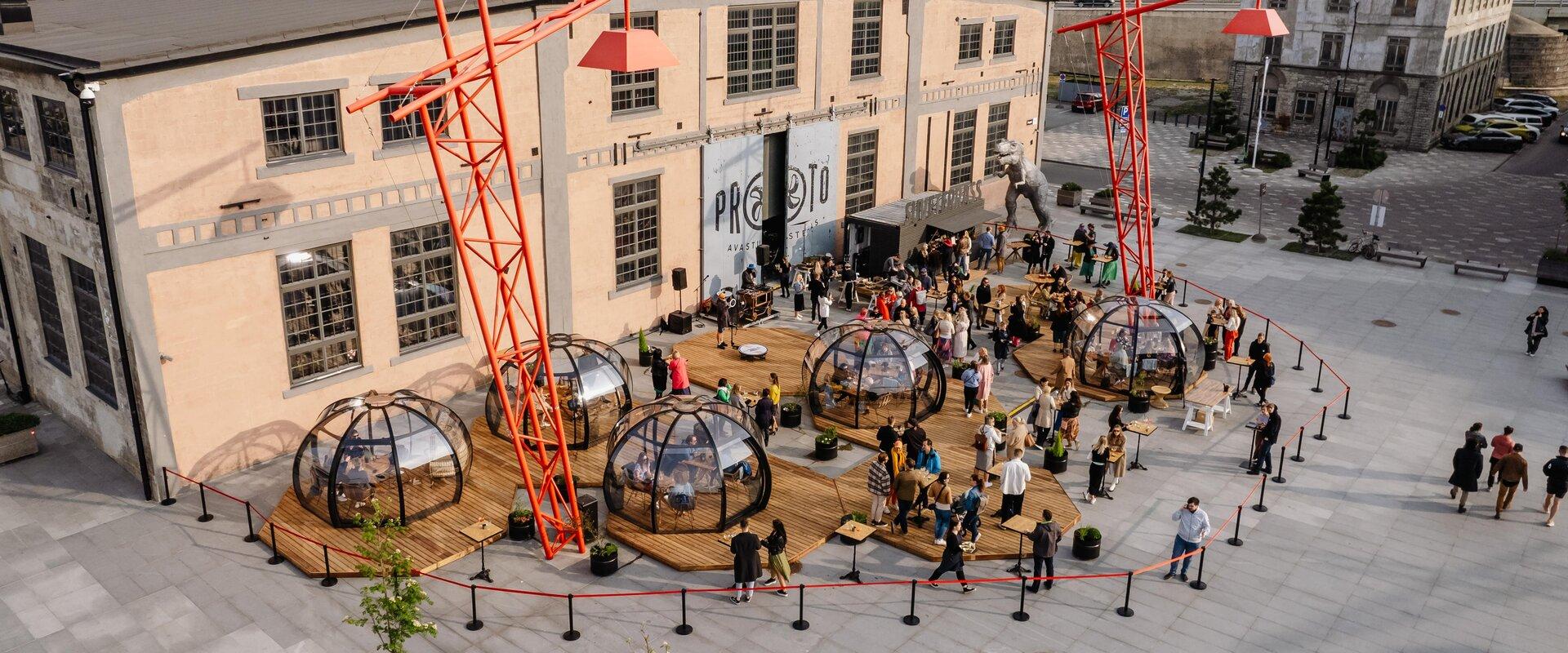 Außenansicht der Sommerterrasse von PROTO – Menschen genießen den Abend auf der Terrasse