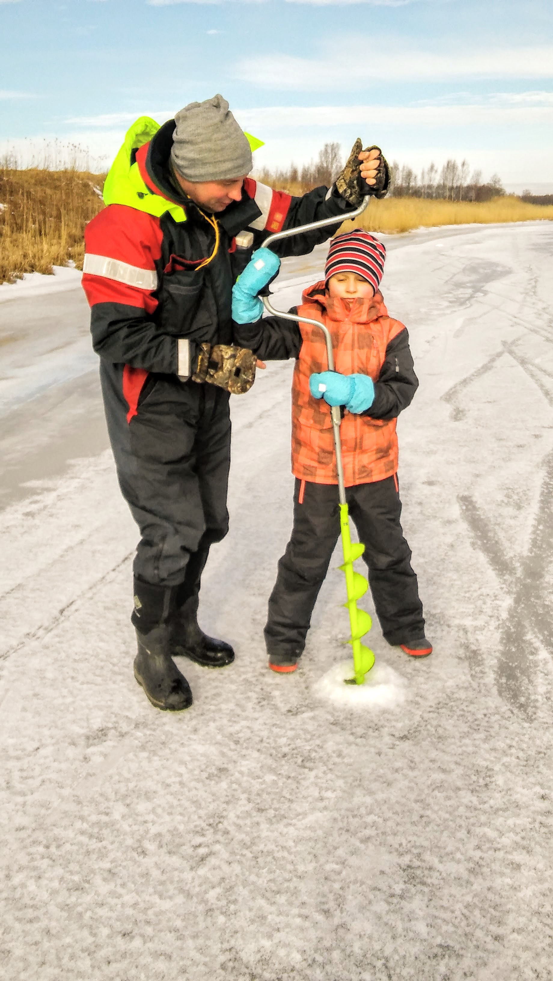 Mees aitab väiksel poisil kalastamiseks jääauku puurida