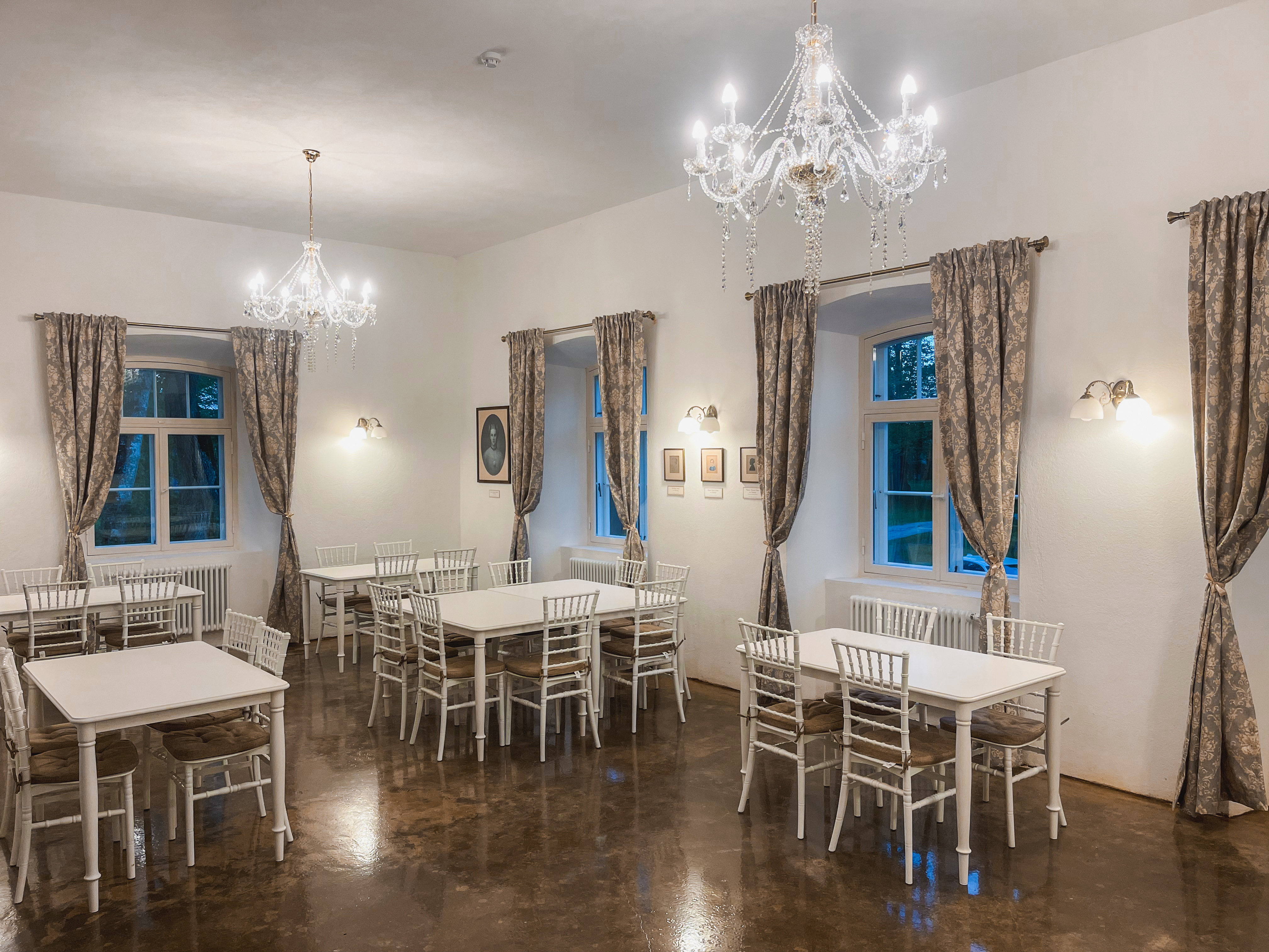 Luke mõisa valitsejamaja elegantne kohviku saal valgete laudade ja lühtritega.