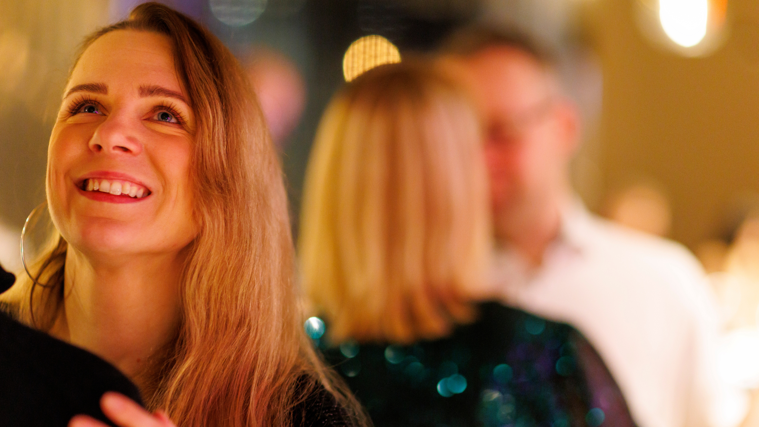 Blond naisterahvas vaatab õnnelikult üles, tantsib noormehega, taustal teised jalakeerutajad.