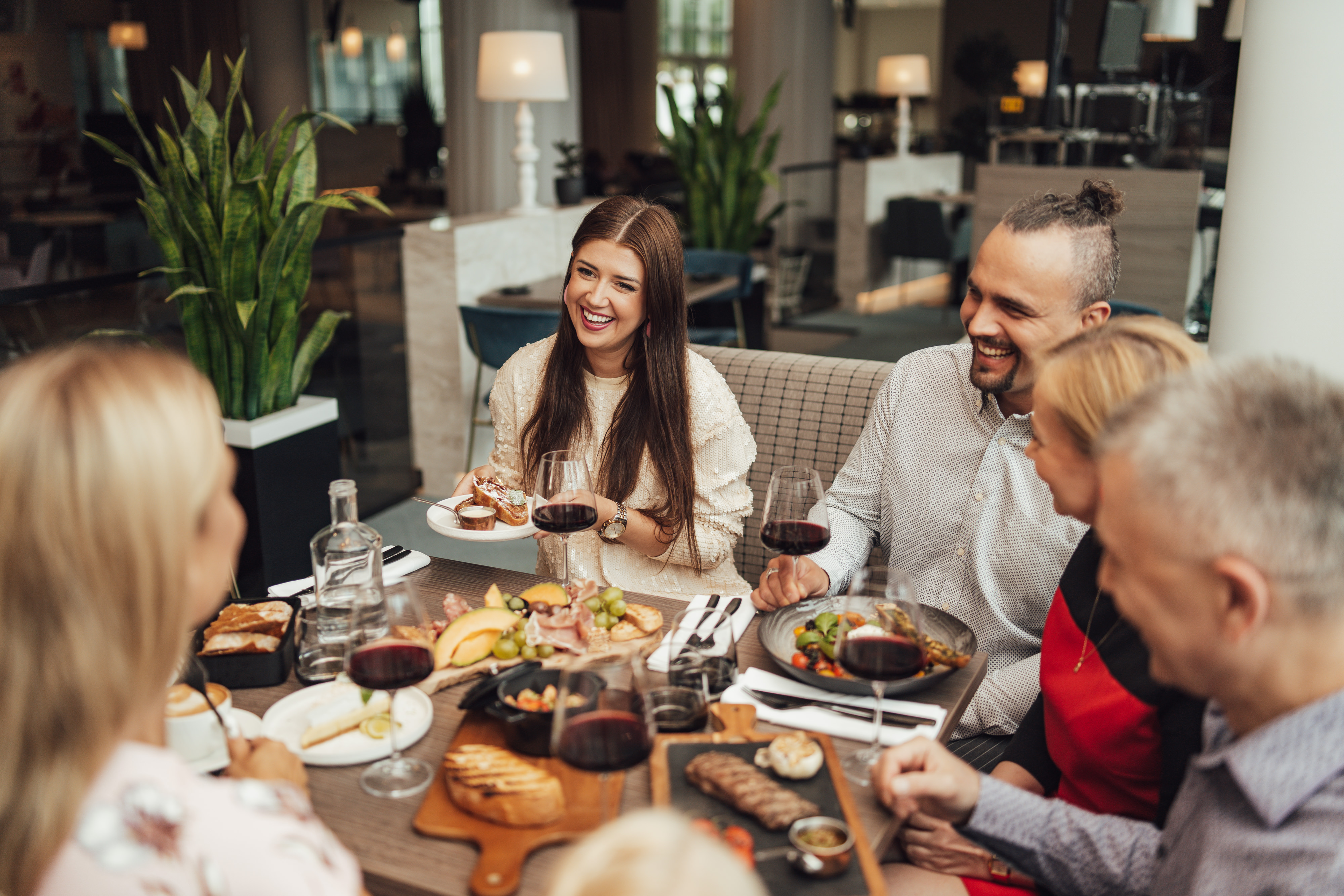 Viieliikmeline perekond istub restoranilauas, kus on näha laia toidu- ja veinivalikut.