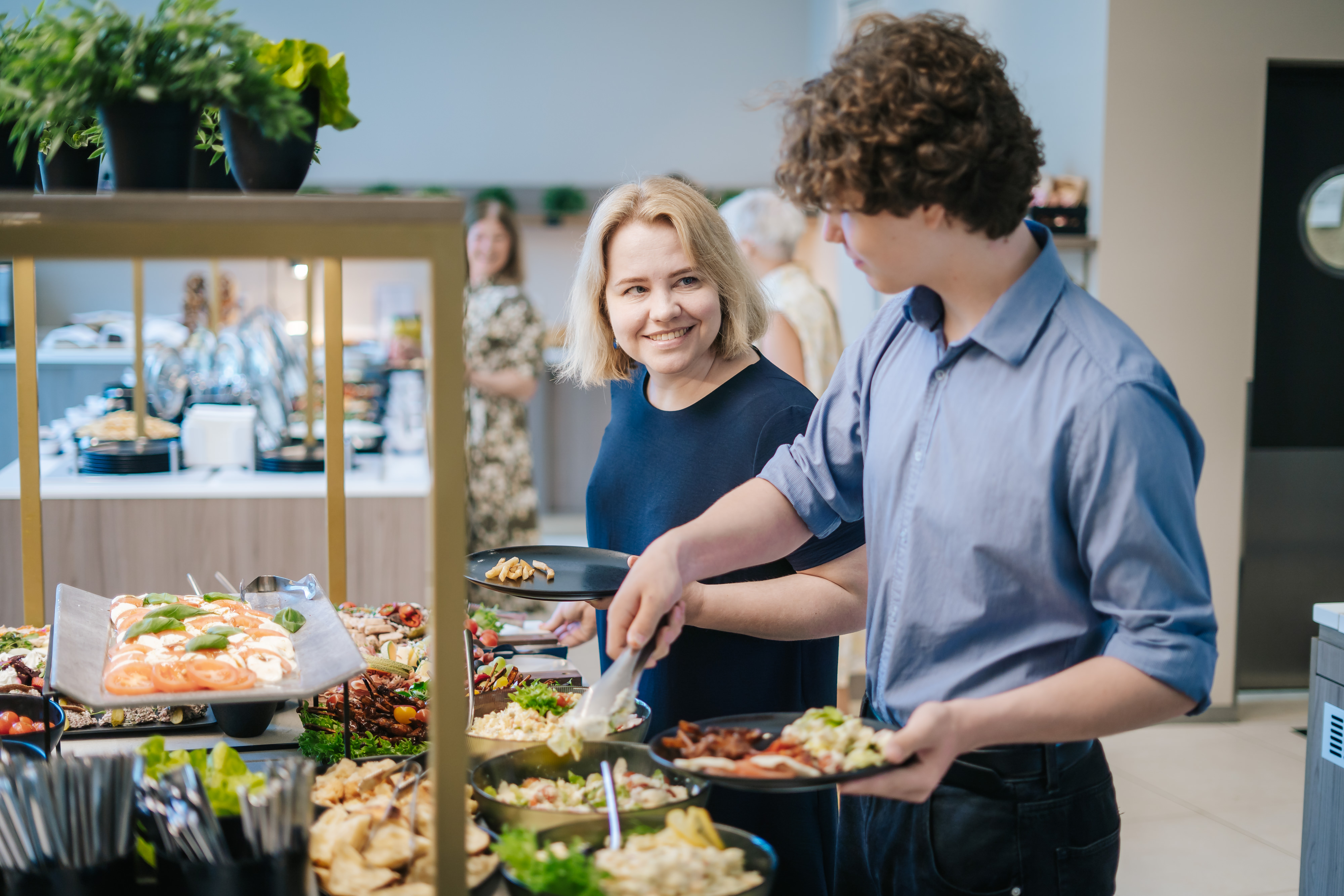 Ema ja poeg tõstavad buffet-lauas endale toitu, mõlemal on seljas sinised pluusid.