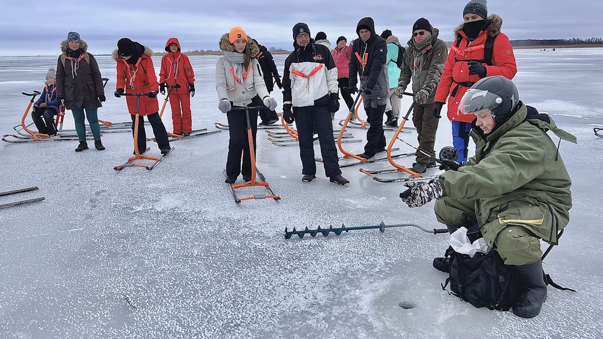 Kick sled trekkers have stopped by the ice hole where a fisherman is fishing for fish.