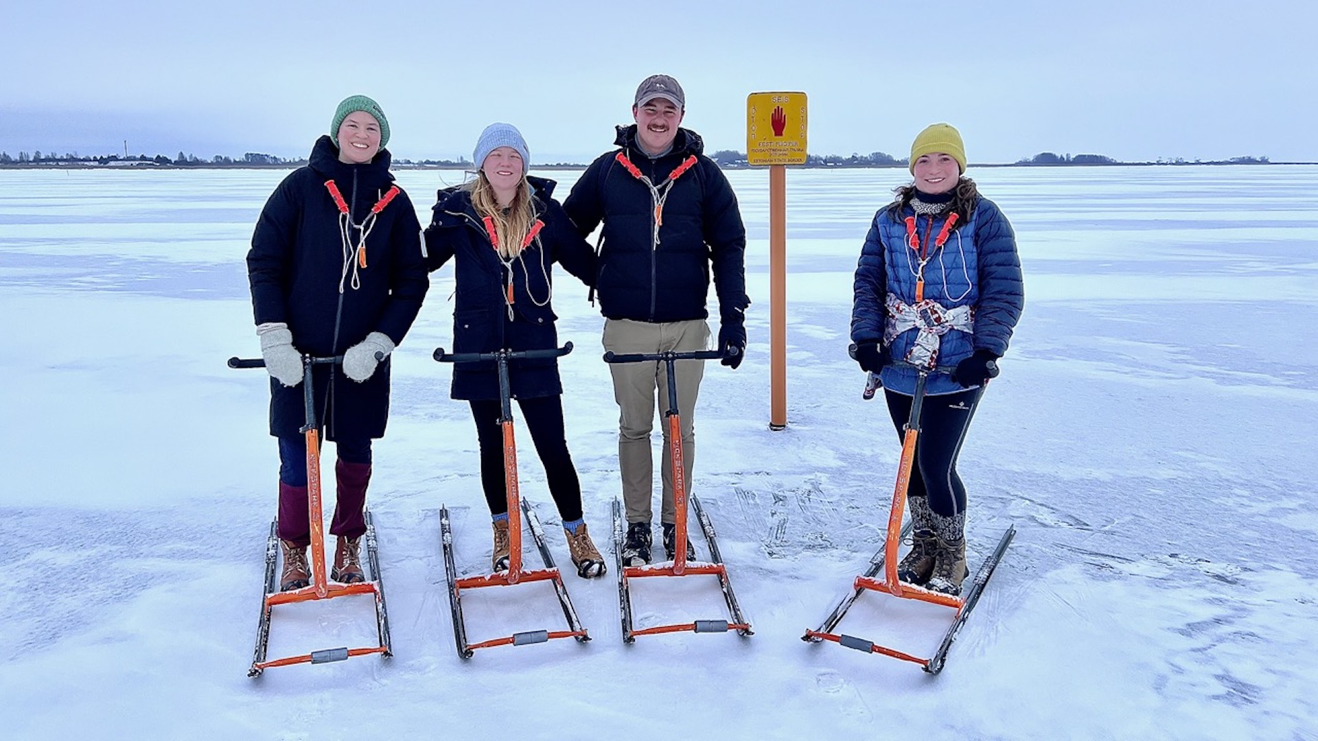 Travelers stand on the lake ice near the Estonia-Russia border warning sign as a group.
