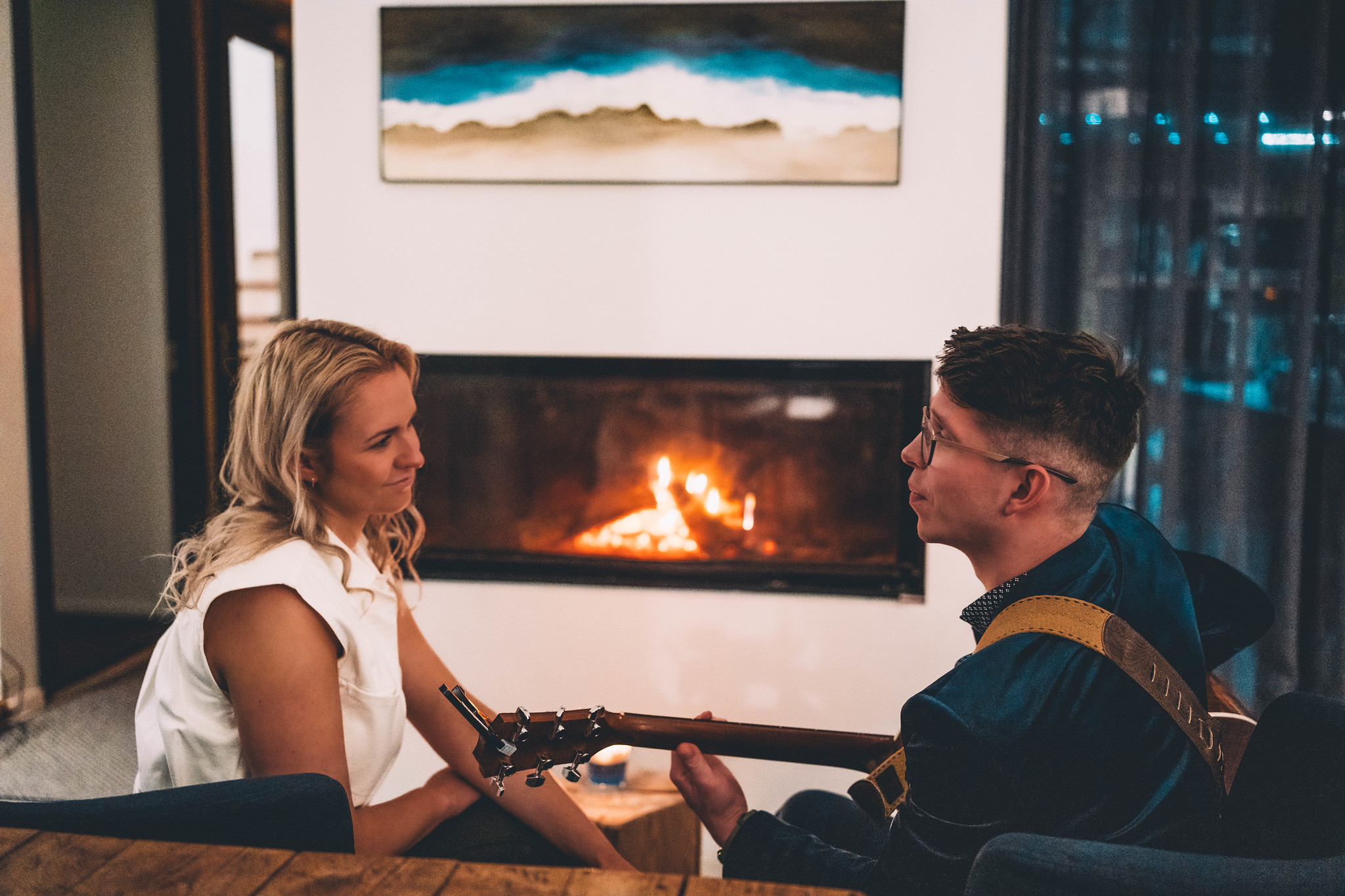 Paar kamina ees kitarri mängimas