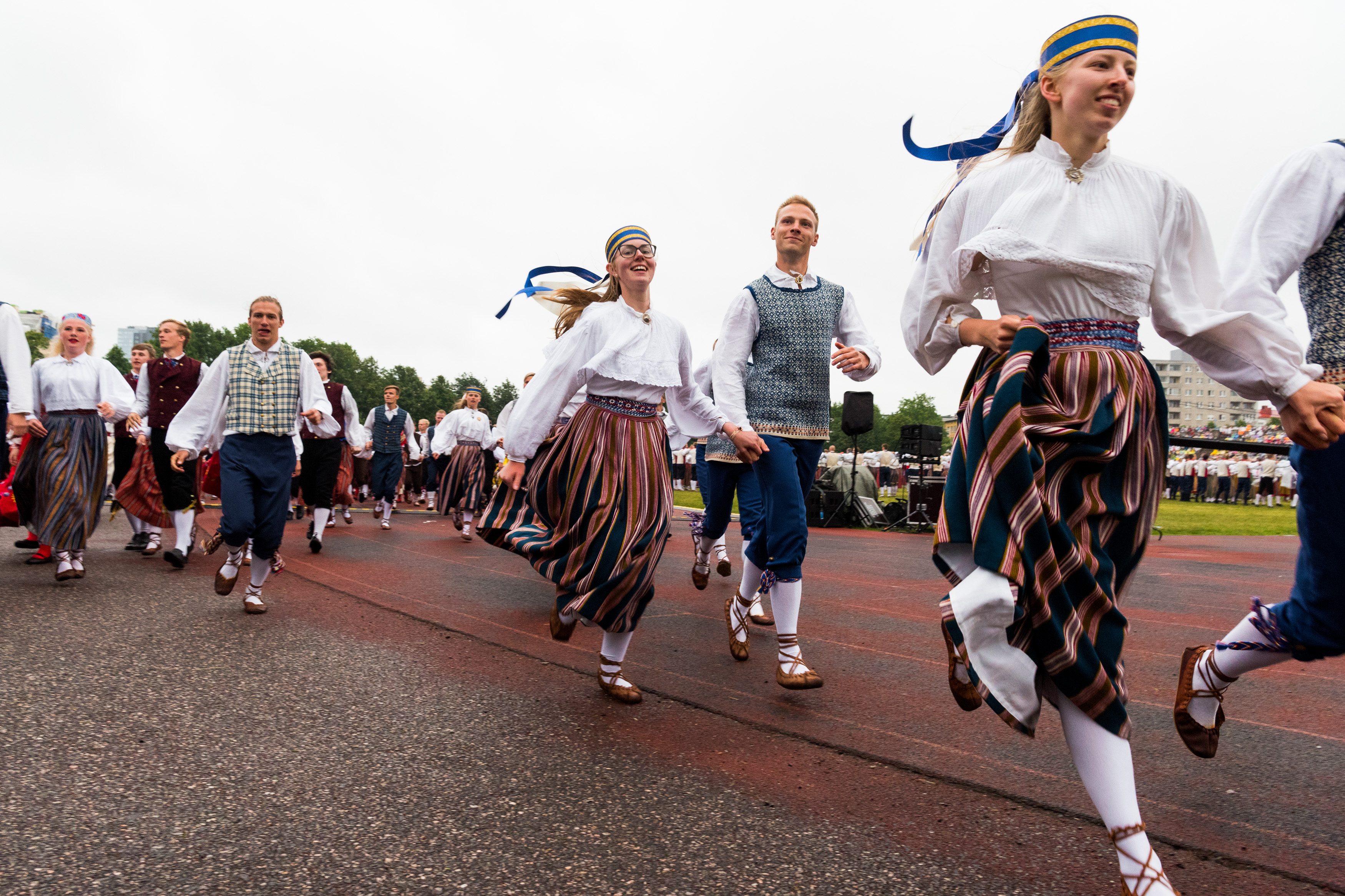 Women and men in Estonian national costumes dance hand in hand.